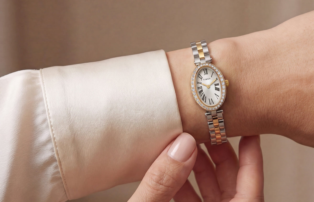 TW2Y90200 Two-tone Timex Cavatina® Crystals watch with a crystal-lined oval bezel and Roman numeral dial, worn beside an ivory blouse cuff.