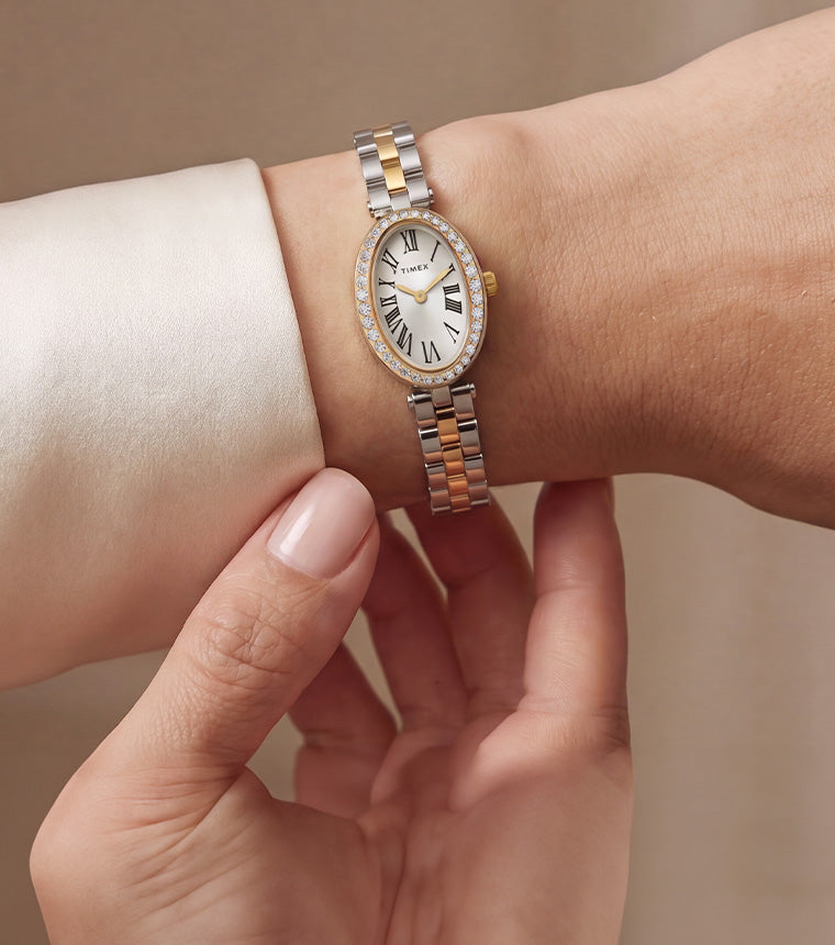TW2Y90200 Two-tone Timex Cavatina® Crystals watch with a crystal-lined oval bezel and Roman numeral dial, worn beside an ivory blouse cuff.