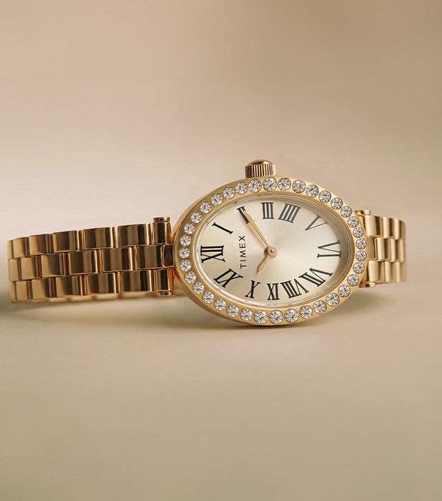 TW2Y90100 Timex Cavatina® Crystals watch with a gold-tone bracelet, champagne oval dial, and crystal-lined bezel on a beige background.