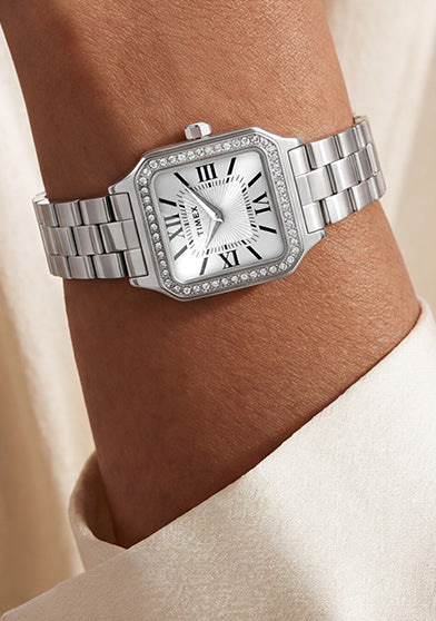 TW2Y90300 Silver-tone Timex Addison watch with a white Roman numeral dial and crystal-lined bezel, worn on a wrist against an ivory blouse.