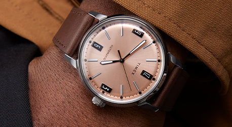 Copper coloured dial watch with a steel case on brown leather strap. Image of watch on wrist. 