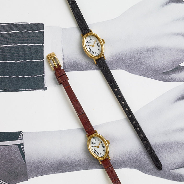Timex Cavatina petite gold-tone oval watches with white Roman numeral dials and leather straps in black and brown, arranged flat on a patterned surface.