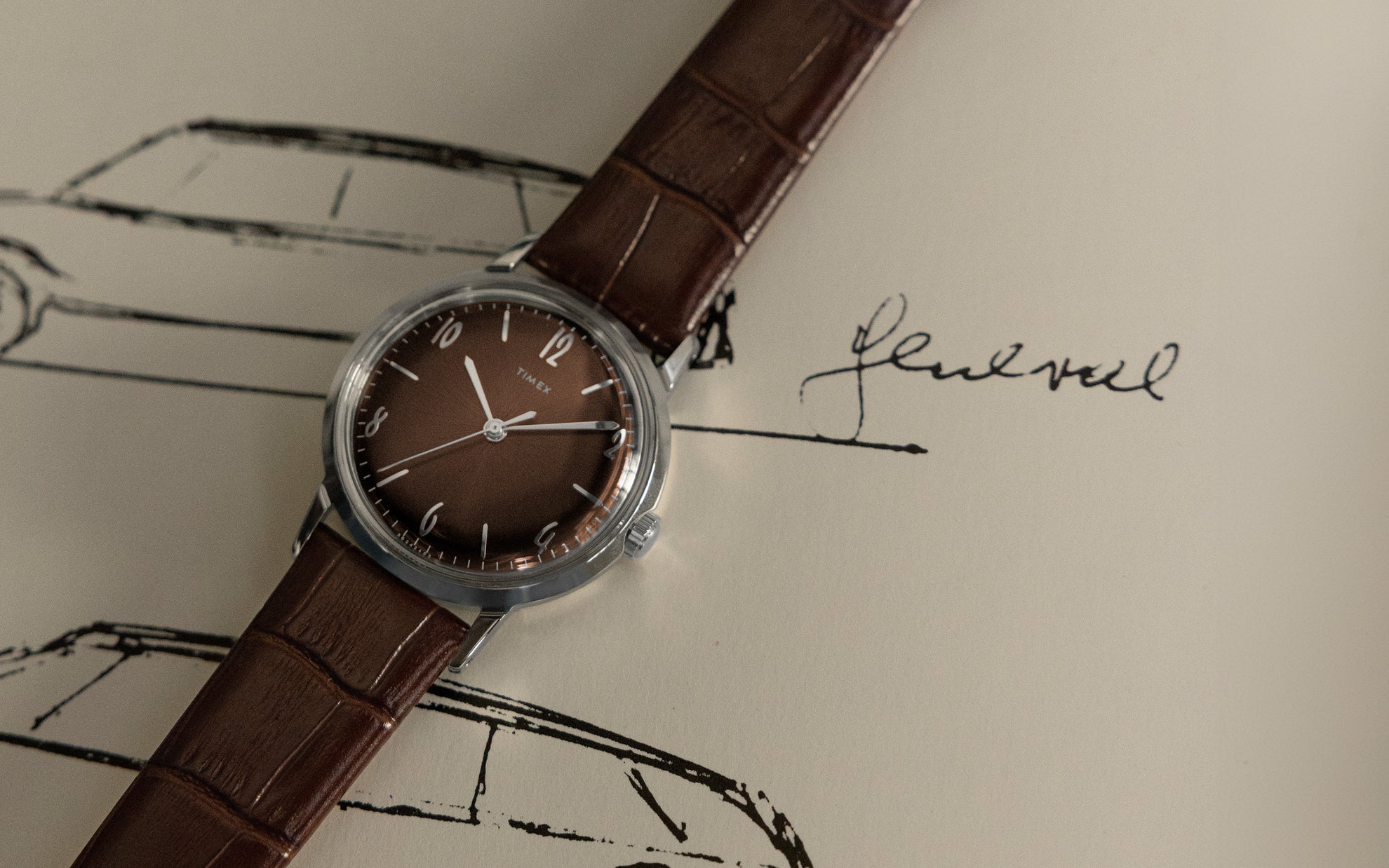 A Timex wristwatch with a brown leather strap and a deep brown dial, placed on a vintage-style sketch of a car with a handwritten signature.