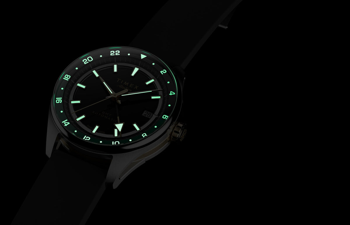 Timex Atelier GMT Première M1a watch glowing in the dark with illuminated hands, hour markers, and 24-hour scale.