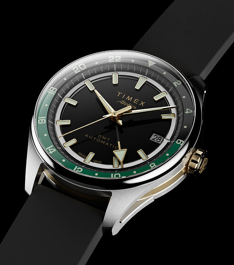 Timex Atelier GMT Première M1a watch with a black dial, green 24-hour scale, gold-tone accents, and black rubber strap.