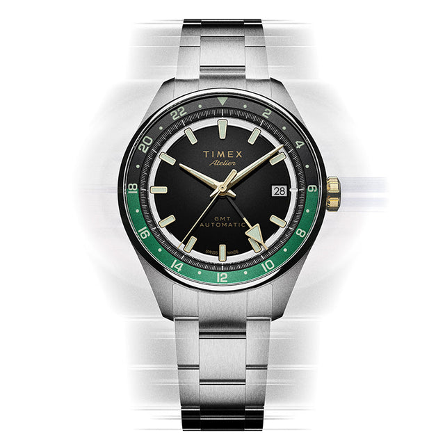 Front view of the Timex Atelier GMT Première M1a watch with a black dial, green GMT scale, and stainless-steel bracelet.