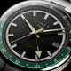 Close-up of the black dial, luminous gold-tone markers, GMT hand, green 24-hour scale, and date window.