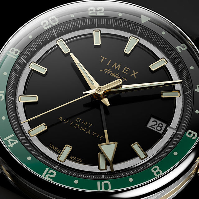 Close-up of the black dial, luminous gold-tone markers, GMT hand, green 24-hour scale, and date window.