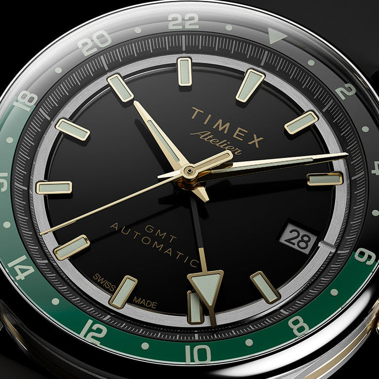 Close-up of the black dial, luminous gold-tone markers, GMT hand, green 24-hour scale, and date window.