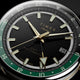 Close-up of the black dial, luminous gold-tone markers, GMT hand, green 24-hour scale, and date window.