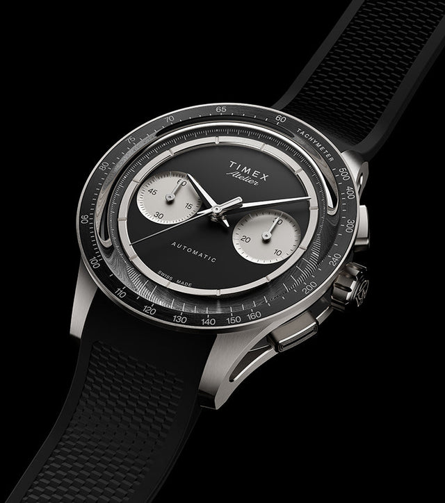Timex Atelier Chronograph Automatic Ti M1a watch with black dial, titanium case, and textured black rubber strap on dark background