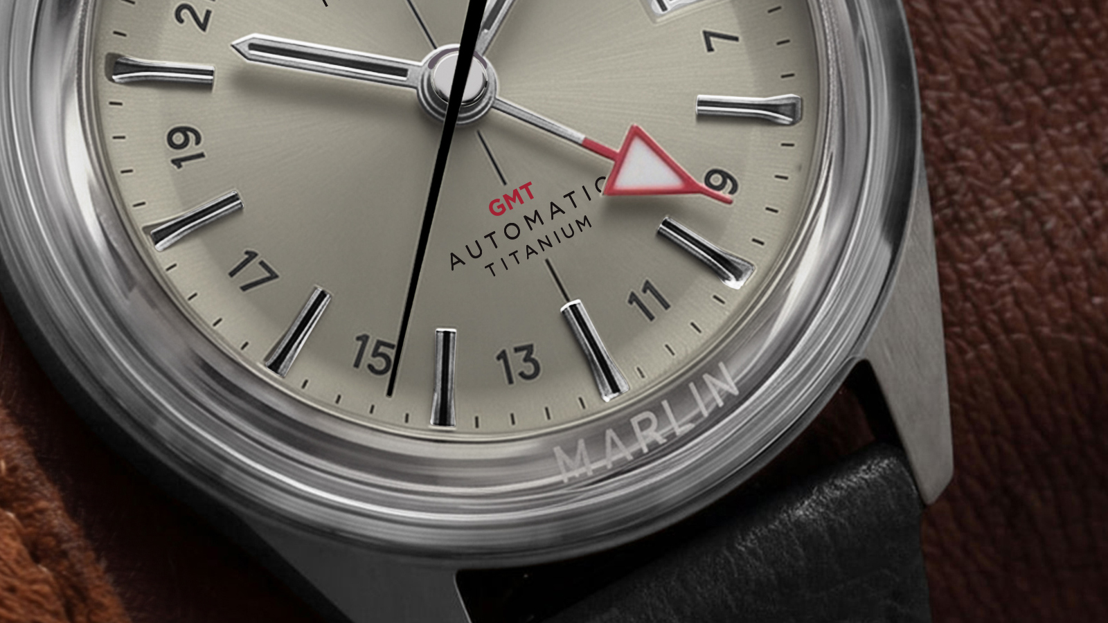 Macro view of the Marlin® Jet Titanium Automatic GMT cream dial, highlighting the red GMT hand, applied hour markers, and Marlin branding on the crystal.