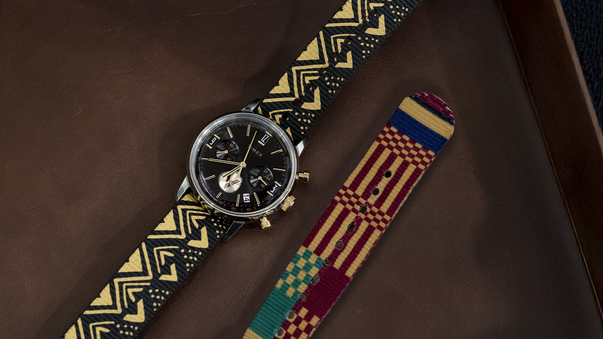 TWG069100 Angled view of the watch and black-and-gold patterned strap laid beside a colorful striped strap.