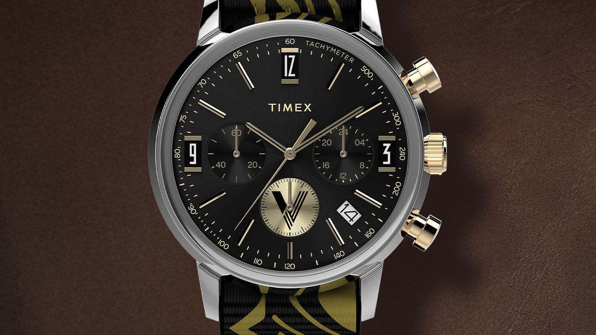 TWG069100 Close-up of the watch’s black chronograph dial, gold-tone hands and accents, and date window.