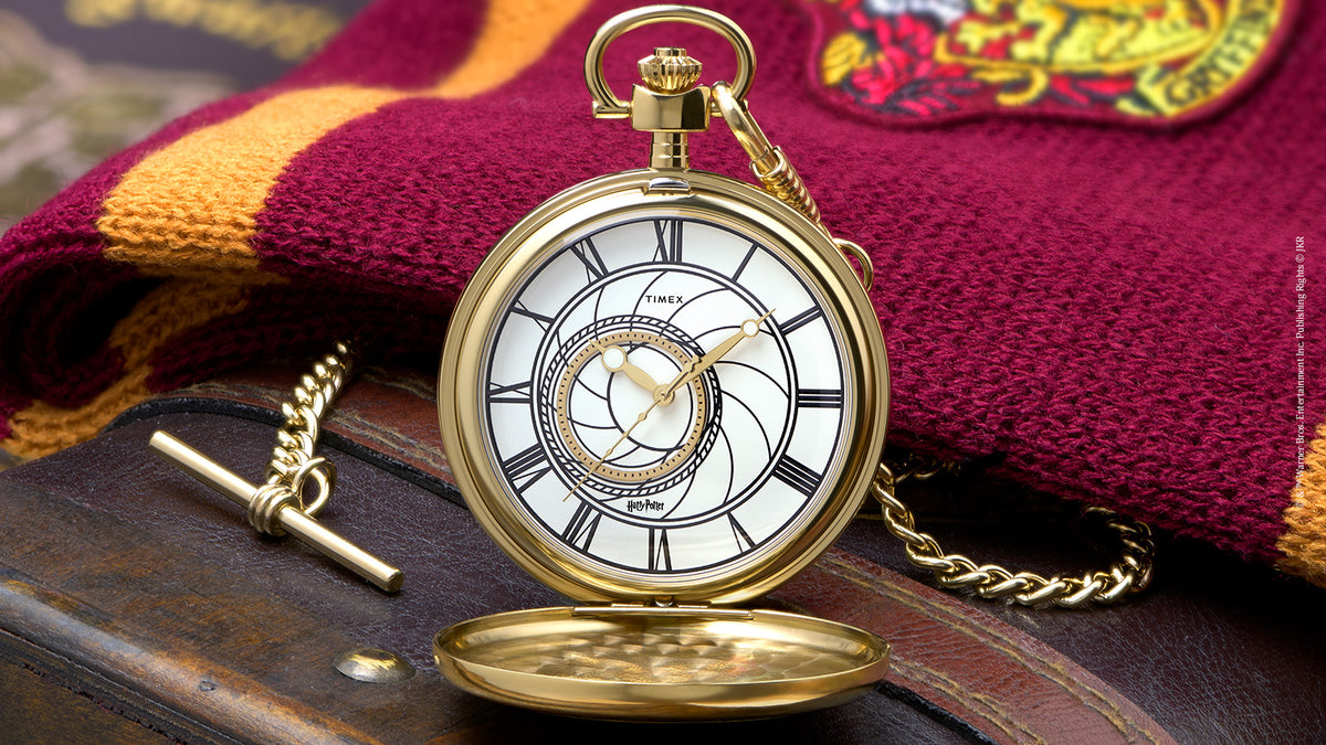 TW2Y99600 Front view of the open pocket watch beside a Gryffindor scarf, showing its white dial, Roman numerals, and chain.