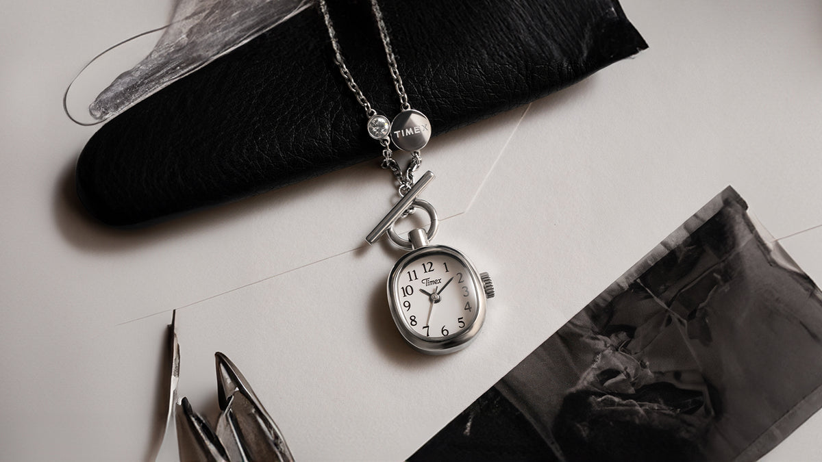 TW6A17600 Cavatina® Mini watch necklace with a white dial and silver-tone case, arranged on paper beside a black leather accessory and photographs.