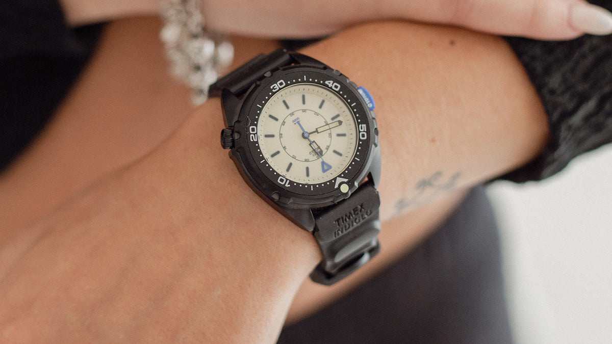 TW6A19800 Timex Intrepid x Dimepiece ‘Blackout’ Edition worn on a wrist, featuring a cream dial and black strap embossed with Timex INDIGLO branding.