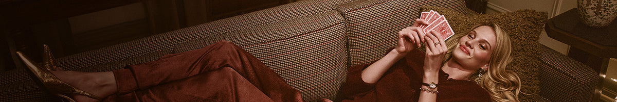 Gifts for Her - Woman reclining on a patterned sofa, holding playing cards and wearing a gold-tone Timex watch.