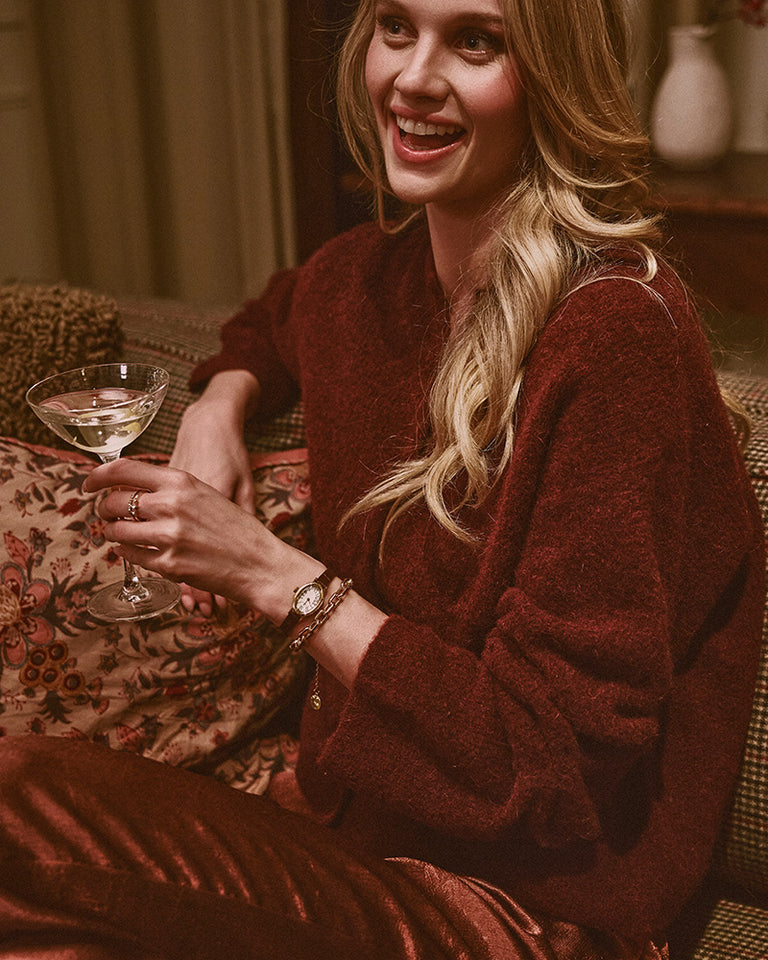Gifts for Her - Smiling woman in a red sweater wearing a gold-tone Timex watch and holding a stemmed glass.