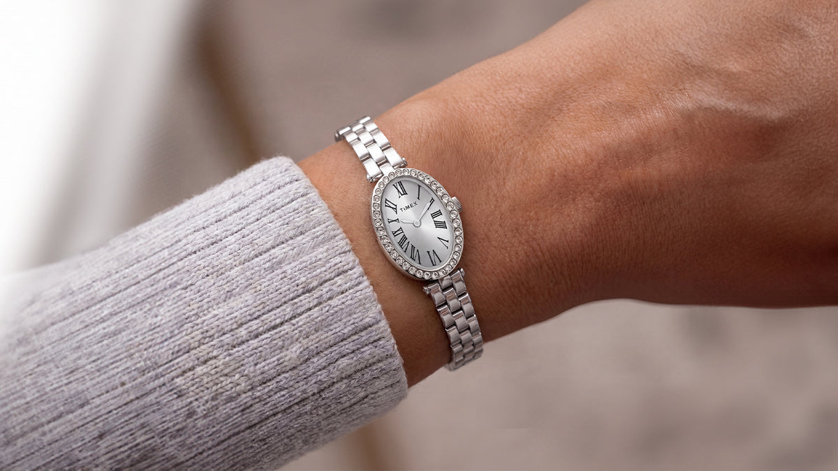 TW2Y90000 Timex Cavatina® Crystals watch worn on a wrist, showing its crystal-lined oval case and slim silver-tone bracelet beside a gray sweater.