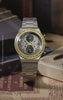 TW2Y75900 Harry Potter x Q Timex Time Turner Chronograph with a gold-tone bezel, star-patterned dial and silver-tone bracelet, displayed beside a Time-Turner necklace, wand, glasses and books.