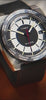 Video showcasing the Timex World Time Reissue watch (model TW2V69500) rotating on an orange leather surface. The footage highlights the brushed stainless-steel case, domed crystal, black-and-white dial with red seconds hand, and engraved world time bezel displaying city names such as New York, Tokyo, and Sydney.