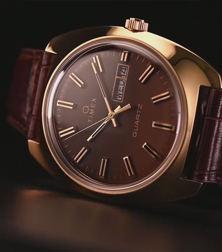 TW2Y87200 Gold-tone watch with a brown gradient dial, day-date display, and brown leather strap against a dark background.