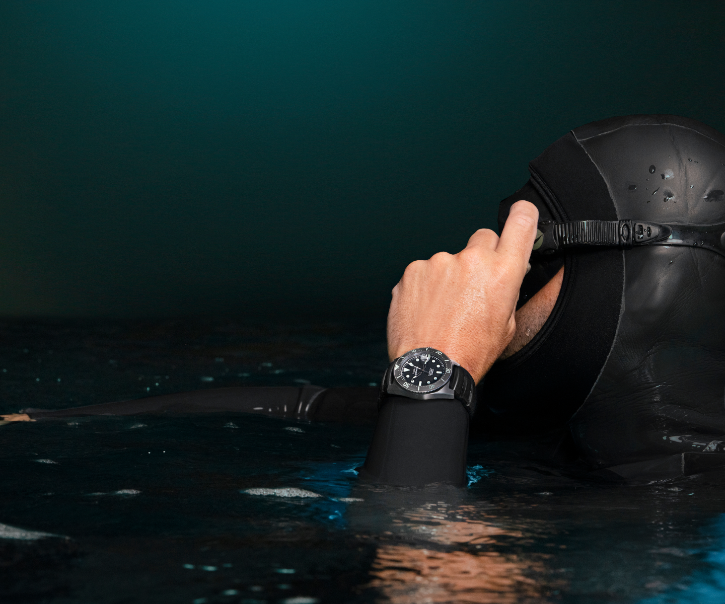 A diver wearing a black wetsuit and diving hood adjusts their mask while partially submerged in dark waters. On their wrist is the Timex Deepwater Reef 200 Titanium Automatic dive watch, featuring a black dial, luminous markers, and a rugged titanium case. The scene is illuminated by subtle ambient light, highlighting the watch’s durability and water resistance. The composition emphasizes the watch as a reliable tool for underwater exploration.